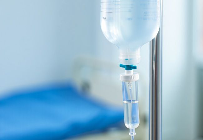 Инфузионный мешок с прозрачной жидкостью и синим регулятором висит на металлической стойке